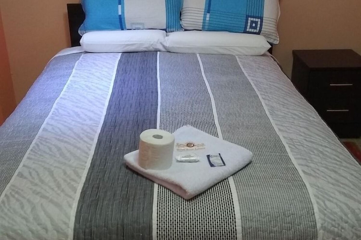 A bed with striped bedding, a pillow, a small bedside table, and a roll of toilet paper.
