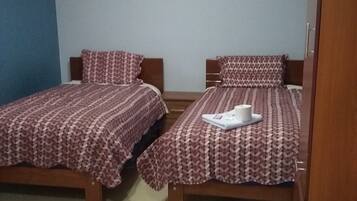 Quarto com duas camas de solteiro, cada uma com roupa de cama e almofadas estampadas, cabeceira de madeira e janela com cortinas.