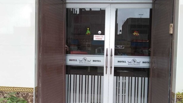 Entrada de hotel con puertas dobles, un letrero que indica 'TOQUE EL TINMBRE' y un cartel con la leyenda 'HOTEL SUITE JULIACA' en la puerta.