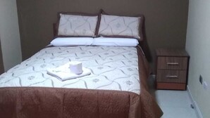 Una cama individual con una colcha marrón, dos almohadas y una mesita de noche con cajón.