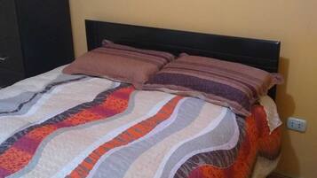 A bed with a patterned bedspread and two pillows, a dark headboard, and a wall socket.