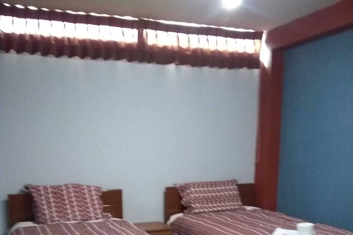 Una habitación con dos camas de madera, cada una con ropa de cama estampada, una mesita pequeña y una silla.