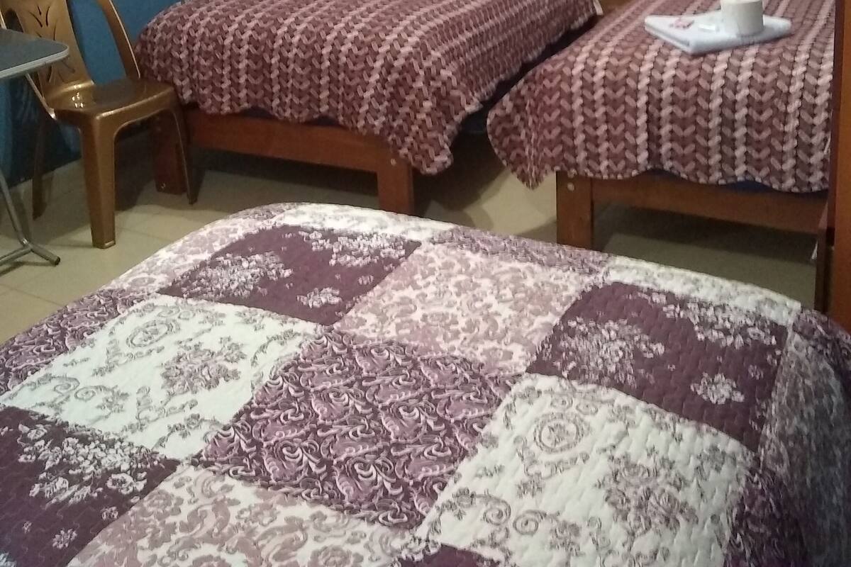 Una habitación con dos camas individuales, una silla de madera y una colcha estampada.