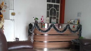 Un salón con un sofá de cuero marrón, un mostrador de recepción de madera con una guirnalda decorativa y una ventana con reja de metal.