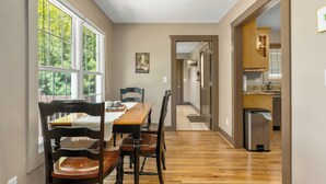 Un espace repas avec une table et des chaises en bois, de grandes fenêtres et une vue sur l’extérieur.