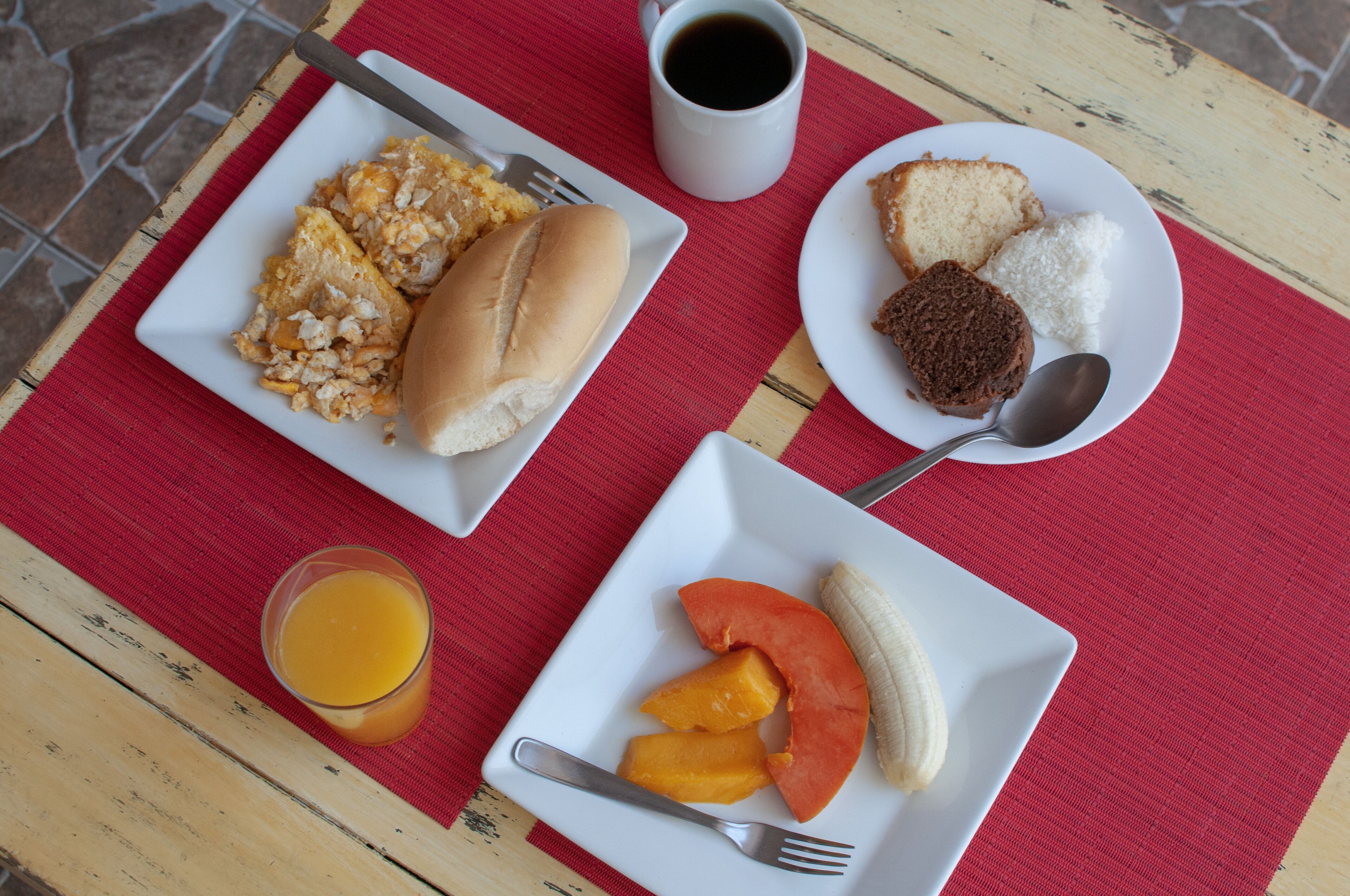 A table with breakfast items including eggs, a bun, toast, a muffin, and fruit.