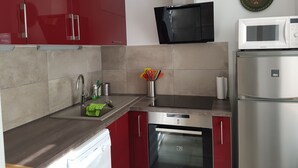A modern kitchen with red cabinets, stainless steel appliances, and a microwave above the oven. - Charming spacious apartment for 4 people (Neuwiller les Saverne)