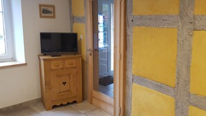 A room with a wooden cabinet, a television, and a door leading to an outdoor area. - Charming spacious apartment for 4 people (Neuwiller les Saverne)