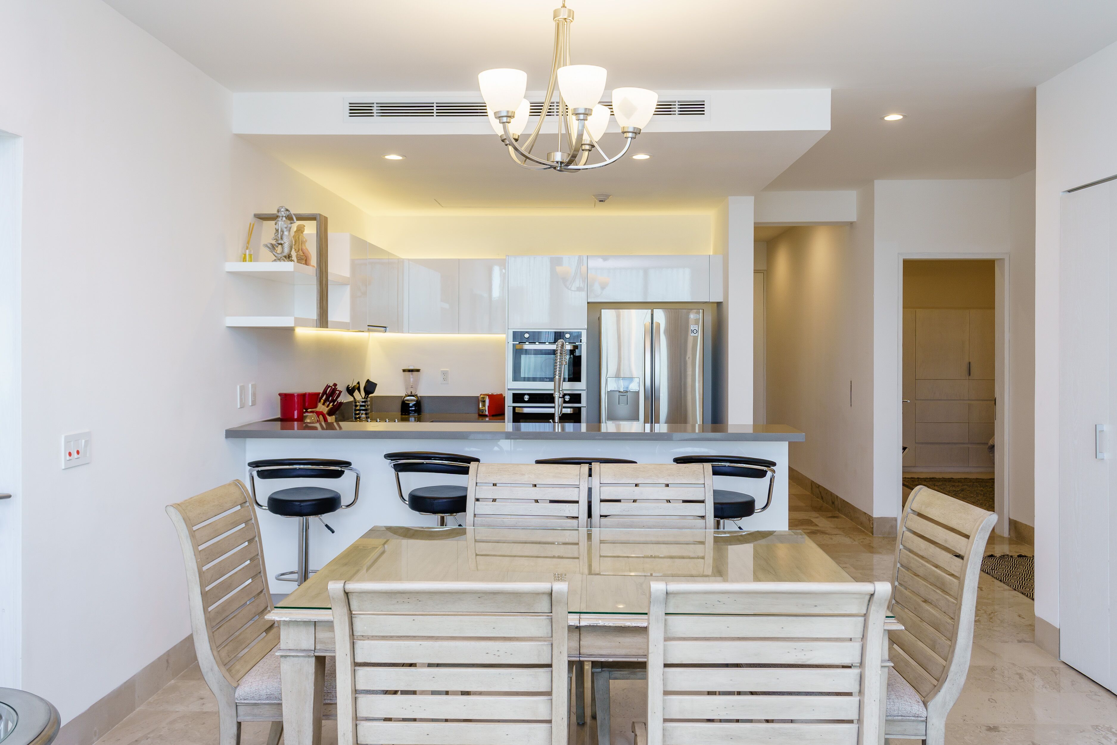 A modern kitchen with a central island, stainless steel appliances, and a dining area with wooden chairs.