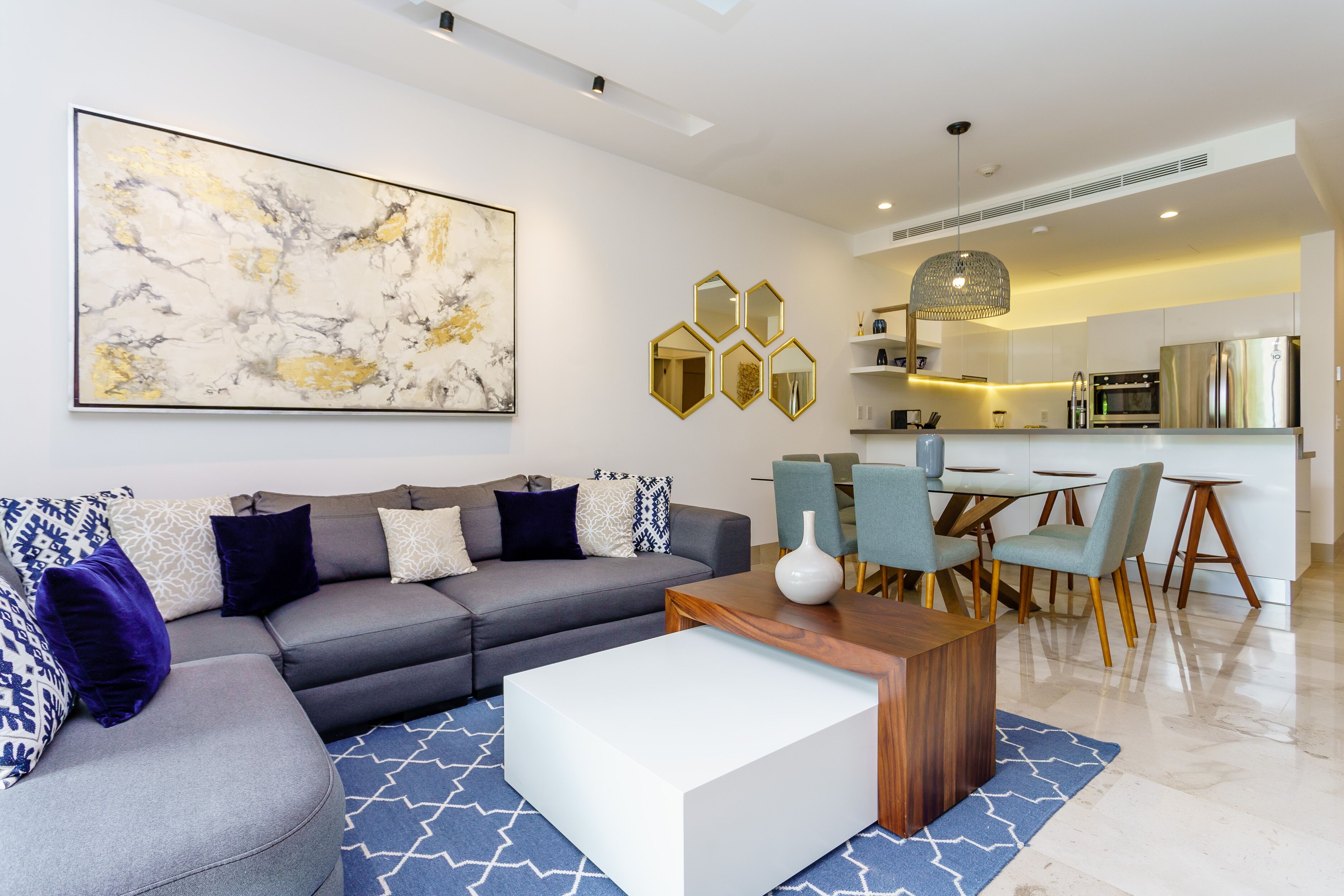 A modern living room with a grey sectional sofa, a white coffee table, and a blue patterned rug.