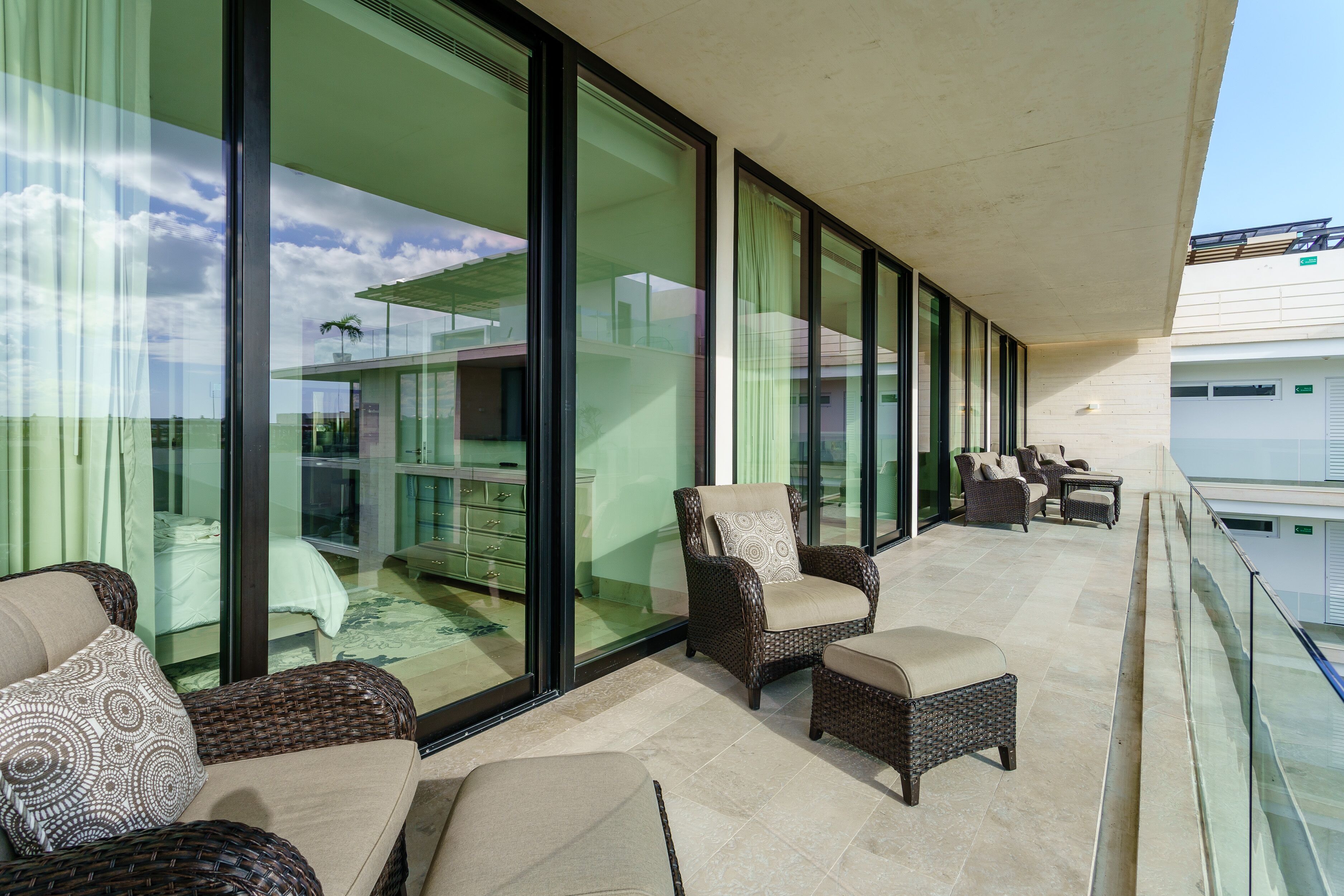 Un balcone con mobili in vimini e una parete vetrata che si affaccia su una zona residenziale.