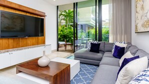 Een moderne woonkamer met een grijze bank, een witte salontafel en een flatscreen televisie bevestigd aan een houten paneel.