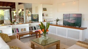 A modern living room with a large flat-screen TV, a glass coffee table, wicker furniture, and a bookshelf with books and decorative items. - TOOL. BUZIOS. (Armaçao dos Buzios)