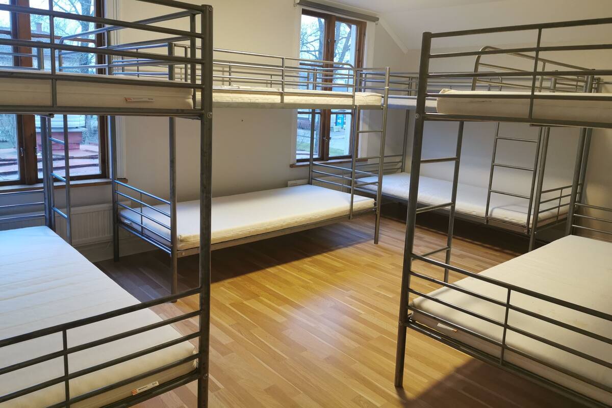 A dormitory room with bunk beds, wooden flooring, and large windows.