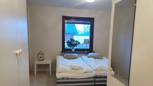 Un dormitorio con cama, mesita de noche y ventana con vista a una casa y árboles.