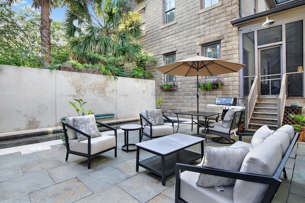 Une terrasse extérieure avec un espace salon, une table et un parasol.