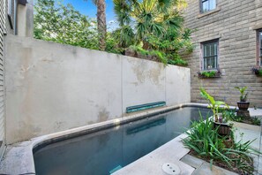 Ein Schwimmbecken mit Betonrand, umgeben von einer Betonmauer und Kübelpflanzen.