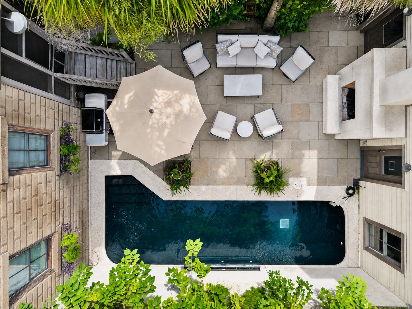 A rooftop pool area with a seating arrangement, a large umbrella, and surrounding greenery.