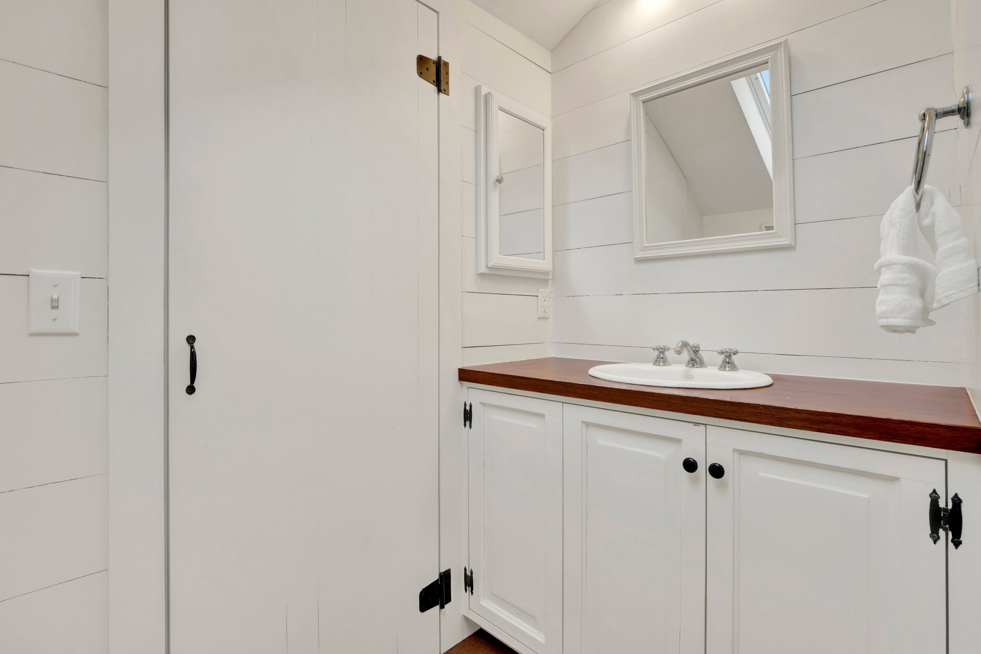 A bathroom with white cabinetry, a wooden countertop, a sink, a mirror, and a towel rack.