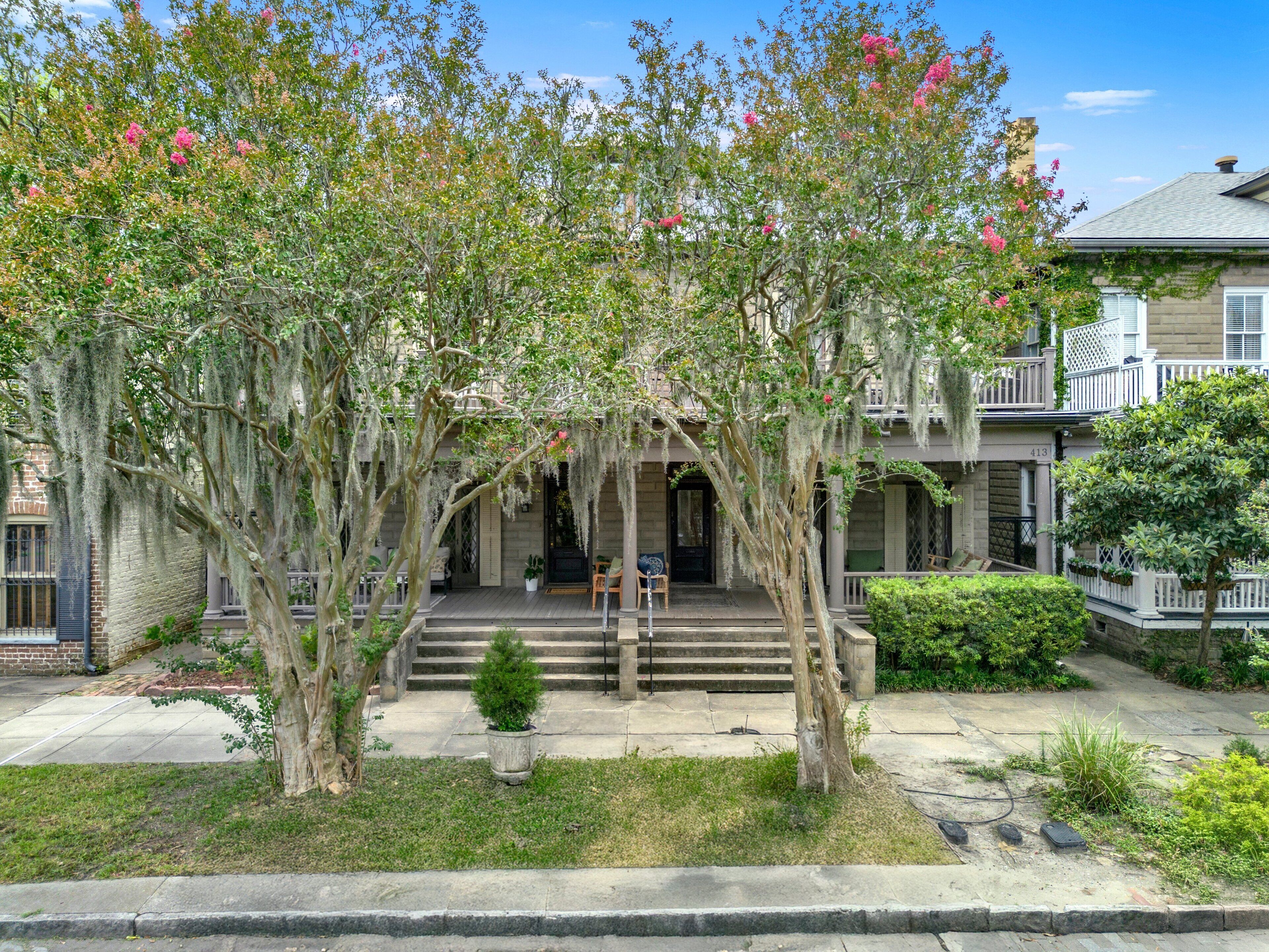 A two-story building with a porch, steps leading up to the entrance, and a small tree in the foreground.