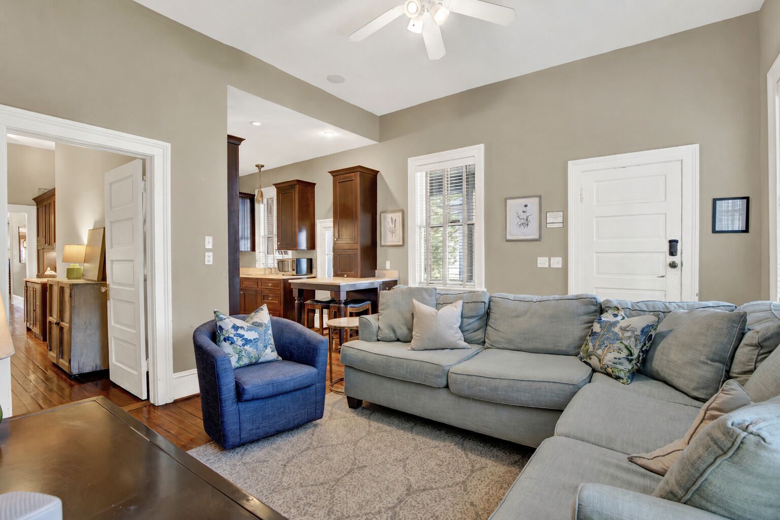 A living room with a sectional sofa, a blue armchair, and a kitchen in the background.