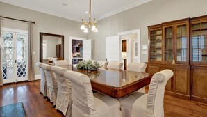 A dining room with a large wooden table, six chairs, a chandelier, and a wooden cabinet with glass doors. - Stately Savannah Home w/ Saltwater Pool (Savannah)
