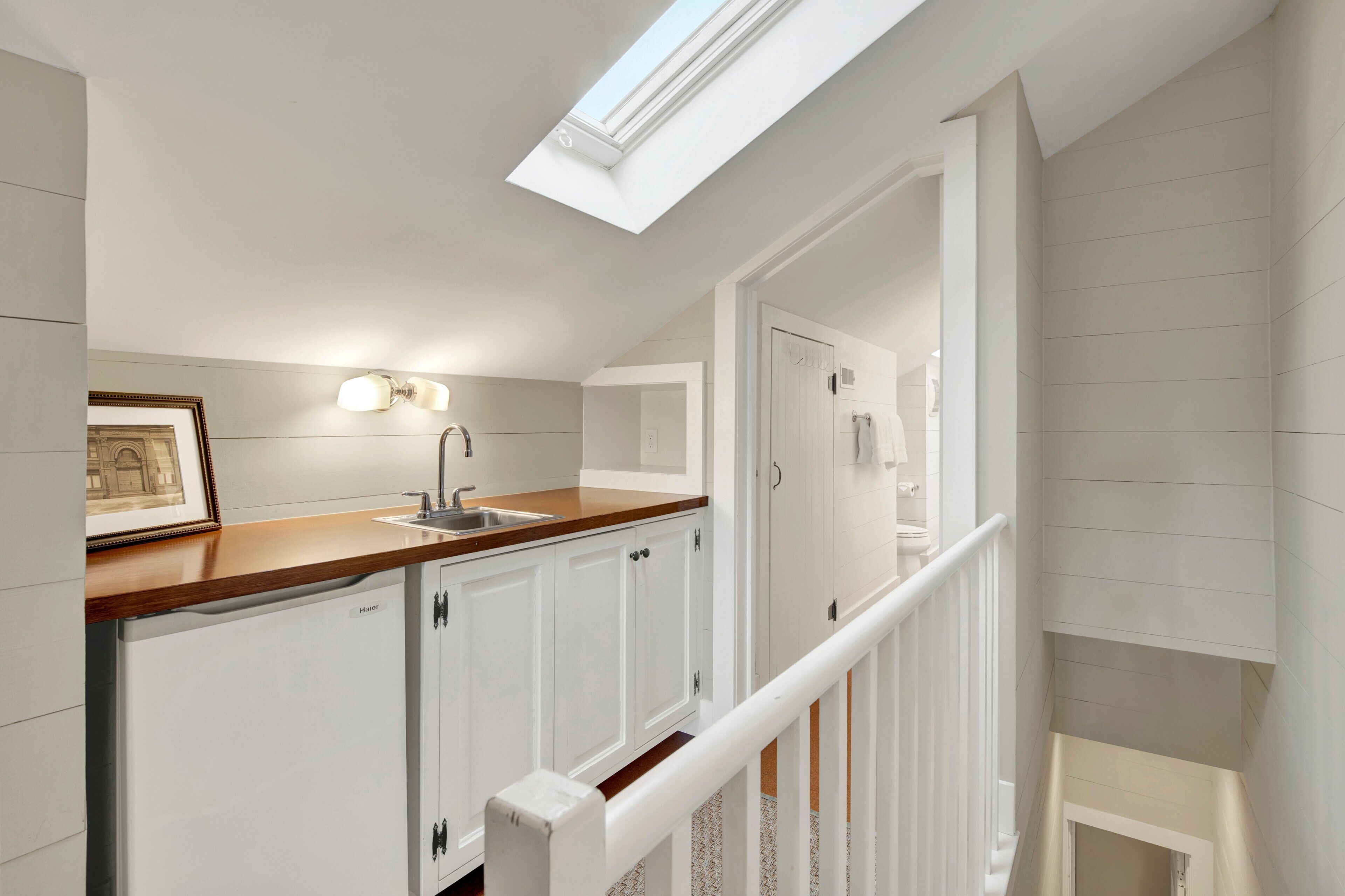 A kitchen with a skylight, white cabinets, a wooden countertop, and a built-in dishwasher.