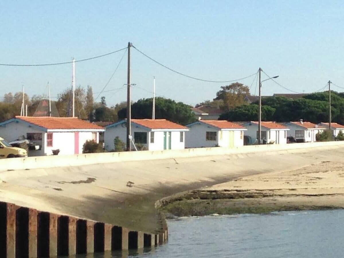 A row of small, single-story houses with red-tiled roofs, situated next to a body of water.