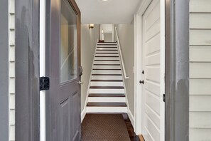 A hallway leading to a staircase with white walls and a brown carpet.