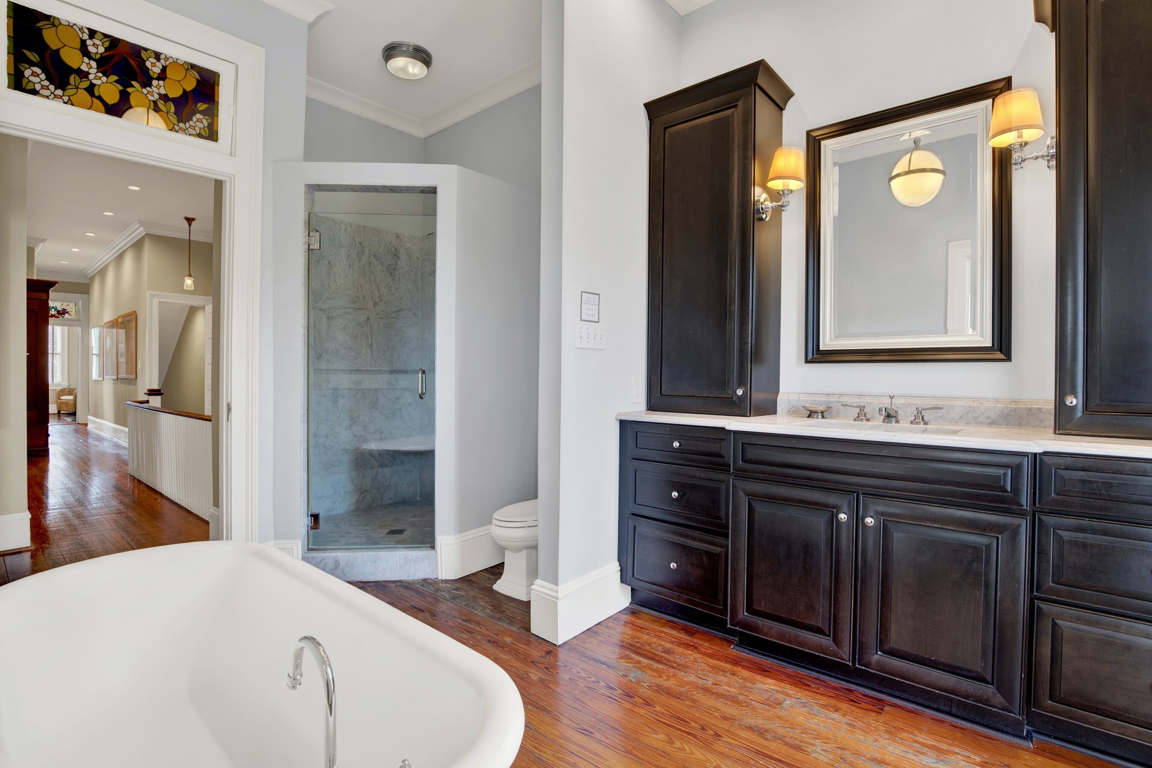 A modern bathroom with a freestanding bathtub, dark wood cabinetry, a large mirror, and a walk-in shower.