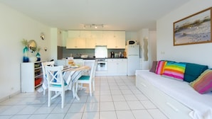 A modern kitchen with white cabinets, a dining area with a table and chairs, and a sofa with colorful cushions. - Appartement Le Chenal in Arès for 4 persons (Arès)