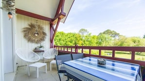 A covered patio with a table and chairs, a decorative wall hanging, and a view of greenery. - Appartement Le Chenal in Arès for 4 persons (Arès)