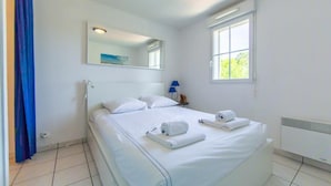 A clean, white hotel room with a large bed, a mirror, a window, and a radiator. - Appartement Le Chenal in Arès for 4 persons (Arès)