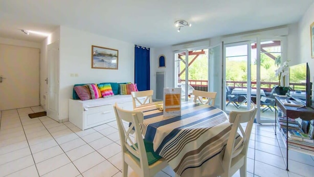 A bright living room with a dining area, a sofa with colorful cushions, a TV, and a balcony with a view. - Appartement Le Chenal in Arès for 4 persons (Arès)