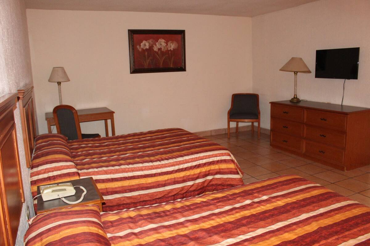 A hotel room with a bed, a desk, a chair, a dresser, and a television.