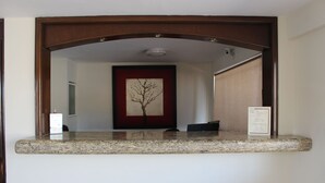 Balcão de recepção com uma obra de arte emoldurada de uma árvore, um pequeno objeto preto no balcão e uma placa com texto.