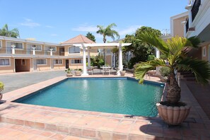 A hotel with a swimming pool, outdoor seating, and palm trees. - Hotel La Villa (Torreón)