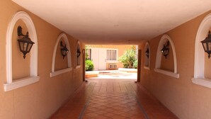 Corredor com piso de azulejos e lanternas fixadas na parede, que leva a uma porta.