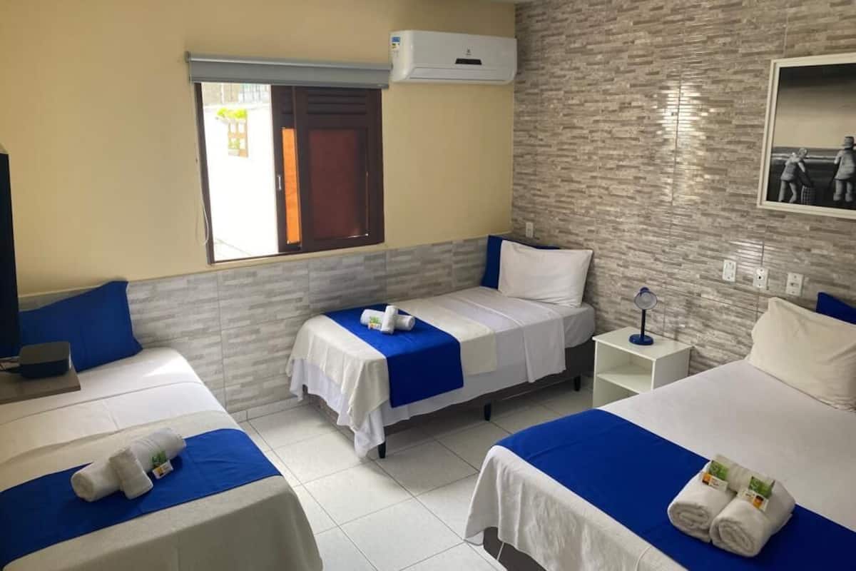 A hotel room with two single beds, a large window, an air conditioning unit, and a tiled floor.