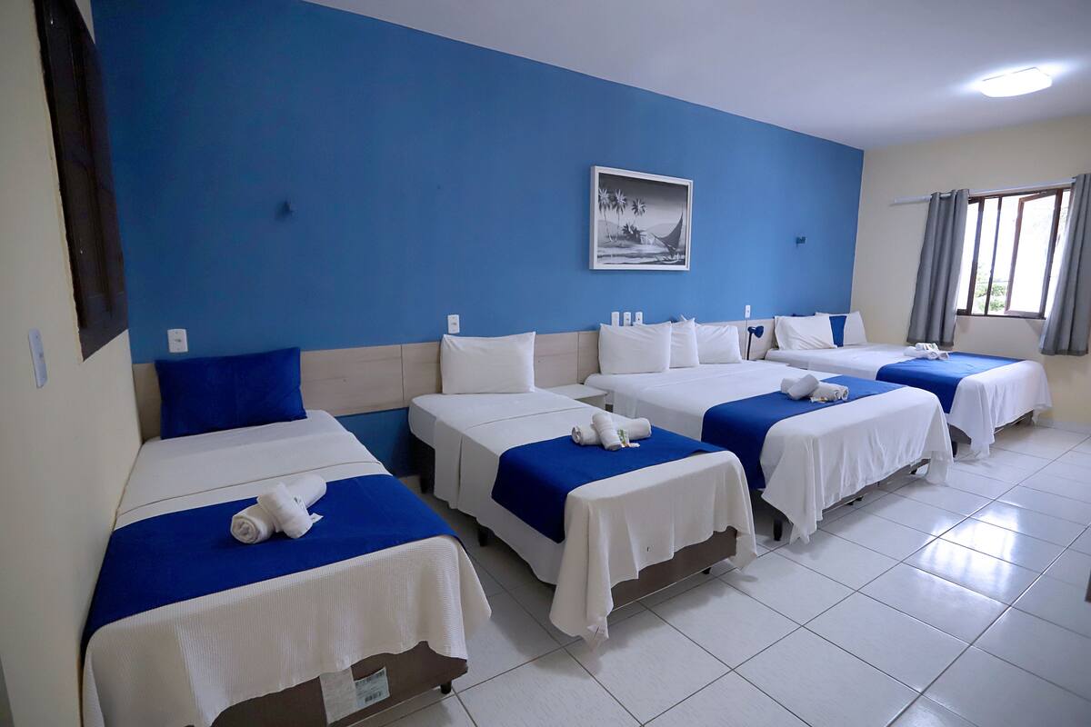 A hotel room with four beds arranged in a row, each with white bedding and blue headboards.