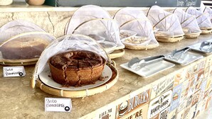 A bakery display with various baked goods, including a chocolate cake, covered in mesh.