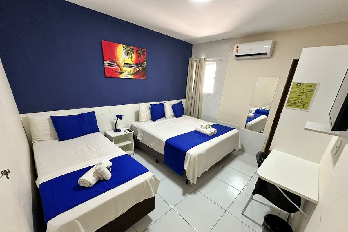 A hotel room with two beds, a painting on the wall, an air conditioning unit, and a desk with a chair.