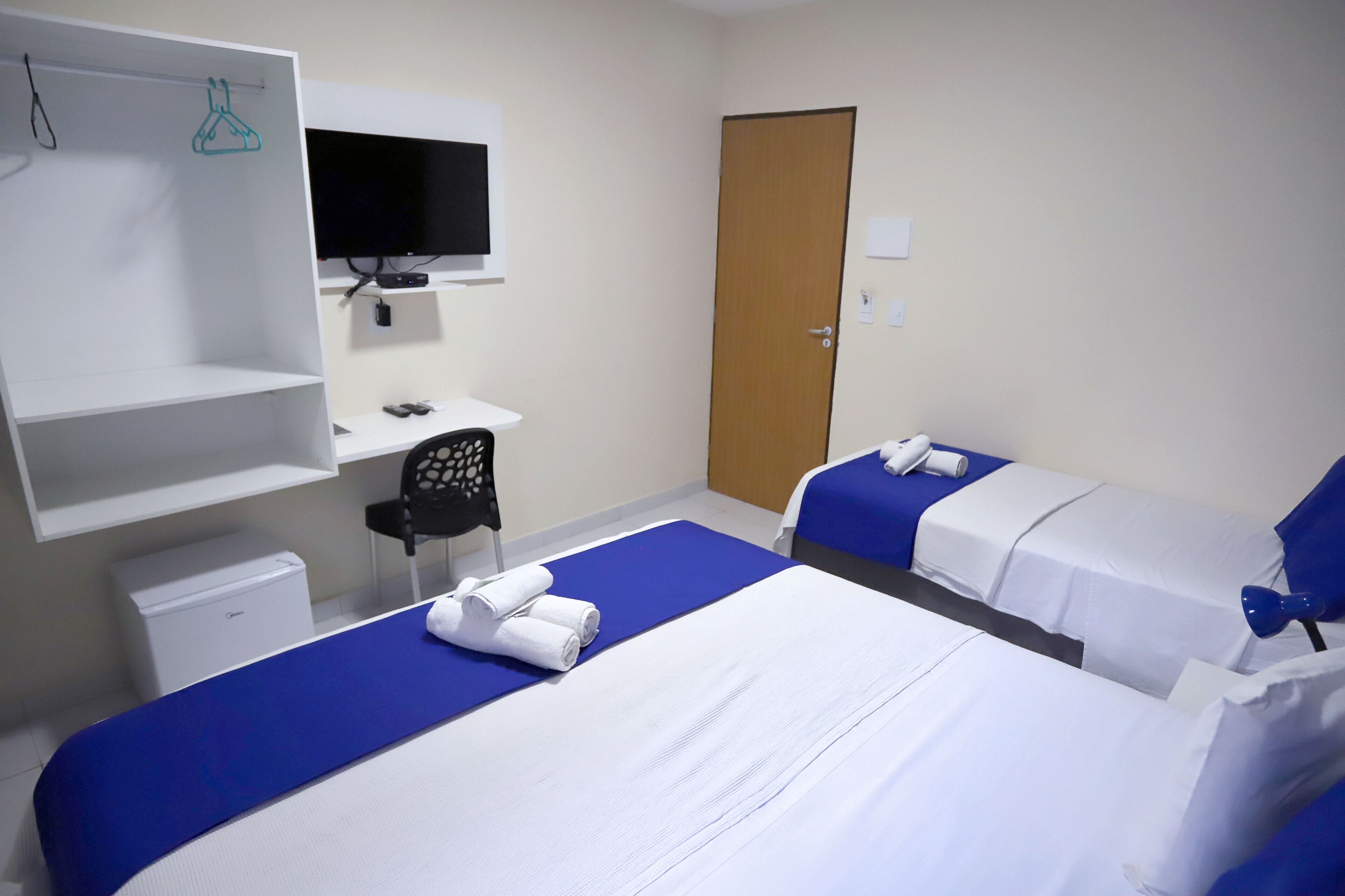 A hotel room with two beds, a desk, a chair, a television, and a wardrobe.