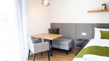 A modern hotel room with a bed, a small table, a bench, and a bedside table.
