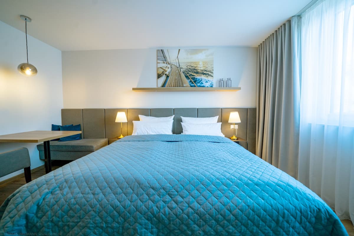 A hotel room with a large bed, two bedside lamps, a desk with a chair, a small table, and a painting on the wall.