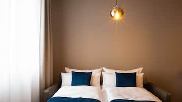 Una cama doble con ropa de cama blanca y azul, un colgante de luz y una pared lisa.