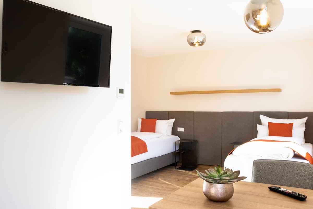 A hotel room with a bed, bedside table, a potted plant, a remote control, and a mounted television.