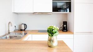 Une cuisine moderne avec des meubles blancs, un évier en acier inoxydable, une bouilloire, une machine à café et un vase rempli de fleurs posé sur le plan de travail.