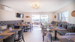 Un espace repas moderne avec de hautes tables et des sièges rembourrés, un téléviseur fixé au mur et de grandes fenêtres offrant une vue panoramique.