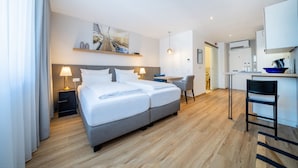 Une chambre d’hôtel moderne équipée d’un lit double, de tables de chevet, d’un bureau et d’une kitchenette.